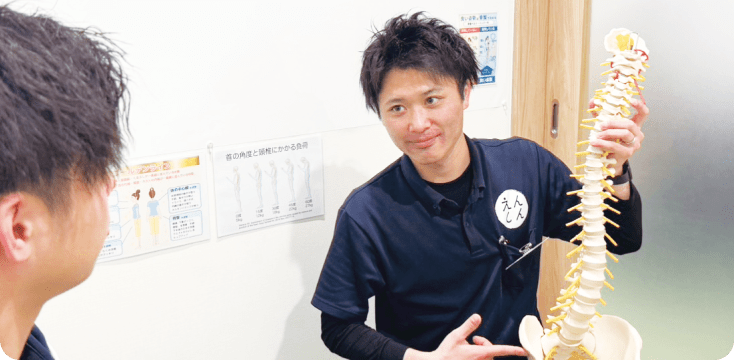 整体師が男性患者に背骨の模型を使って説明をしている場面