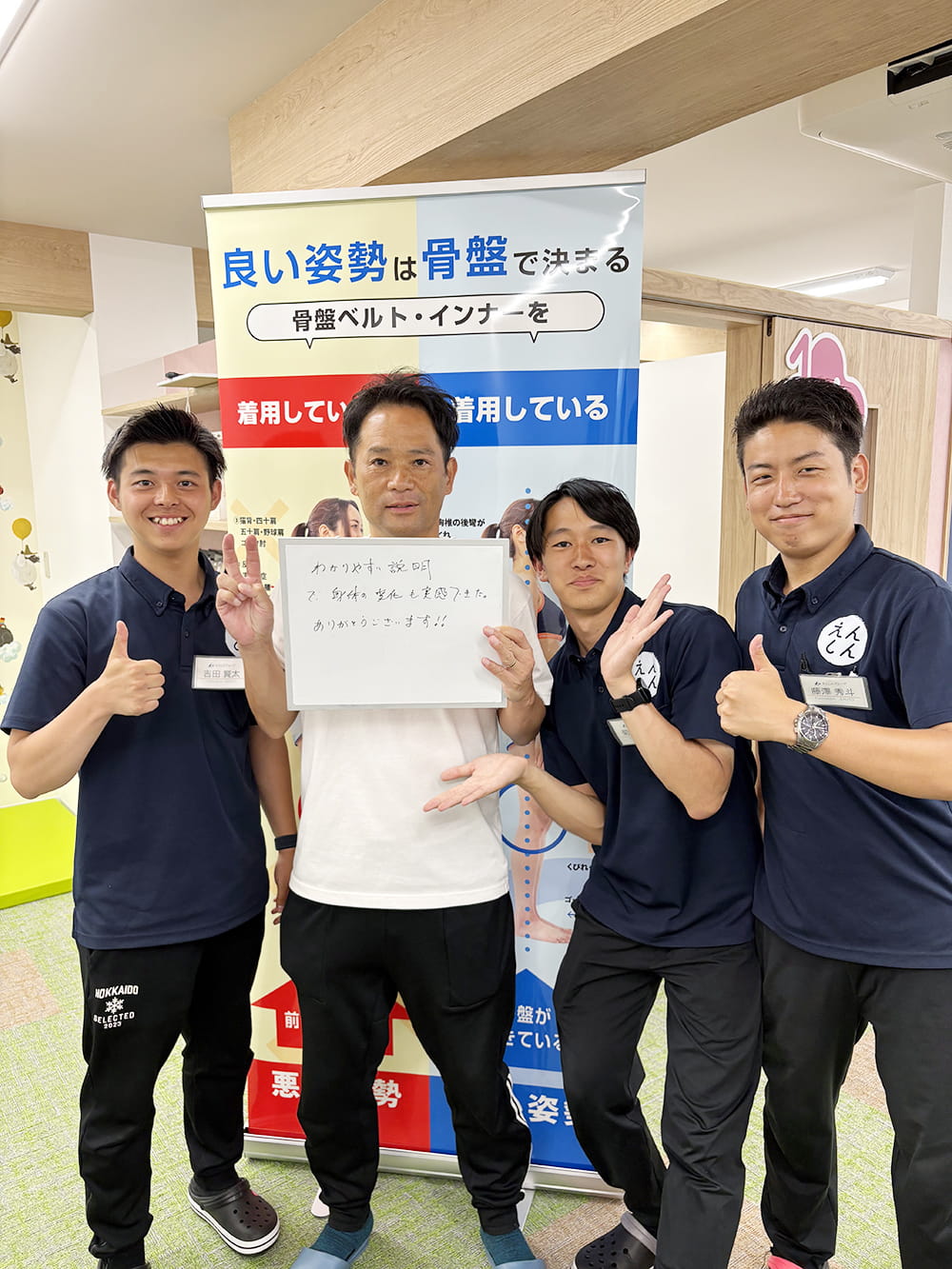 施術後の感想パネルを手にした患者が、制服姿のスタッフと笑顔で記念撮影している様子