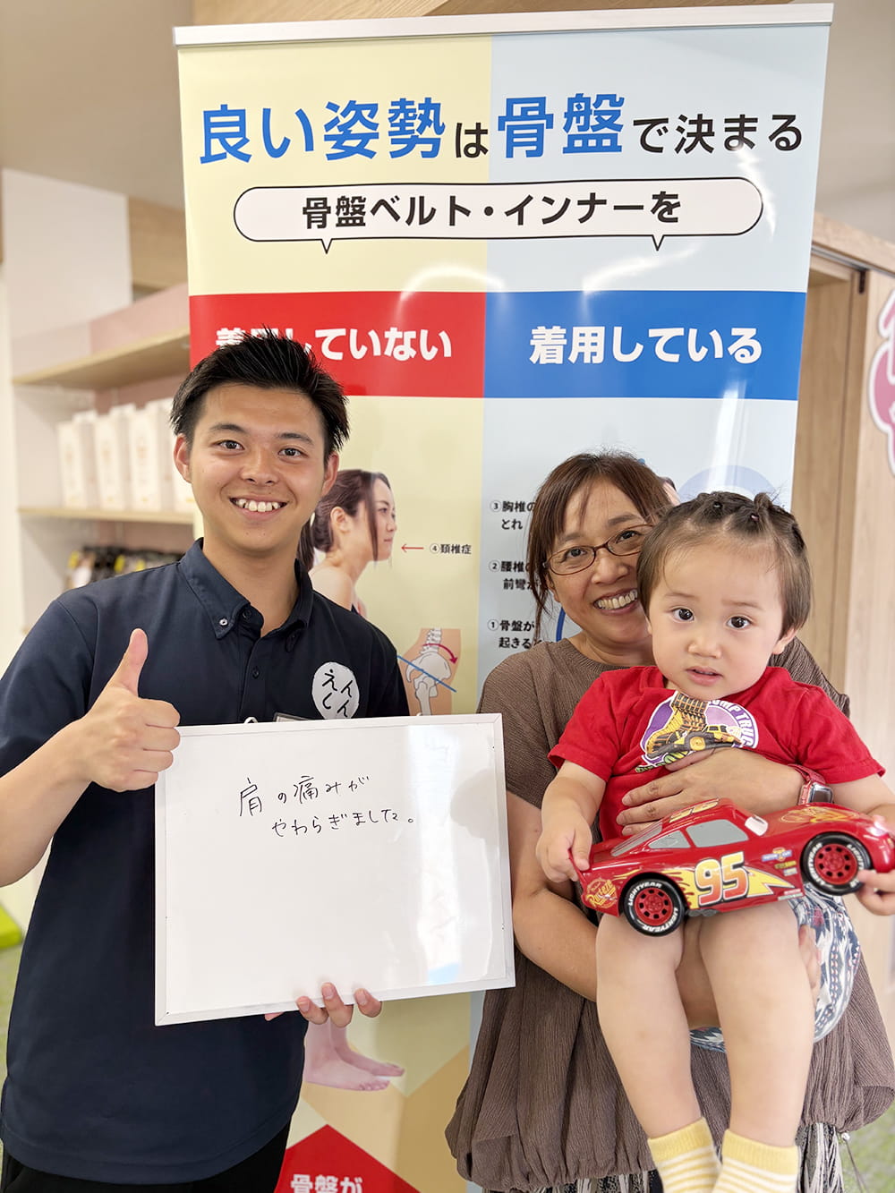 施術後の感想パネルを手にした患者が、制服姿のスタッフと笑顔で記念撮影している様子