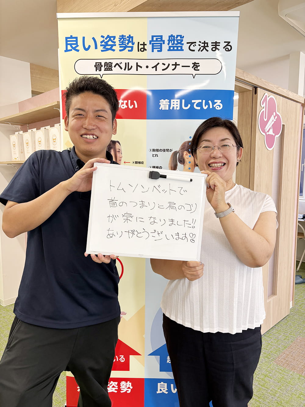 施術後の感想パネルを手にした患者が、制服姿のスタッフと笑顔で記念撮影している様子