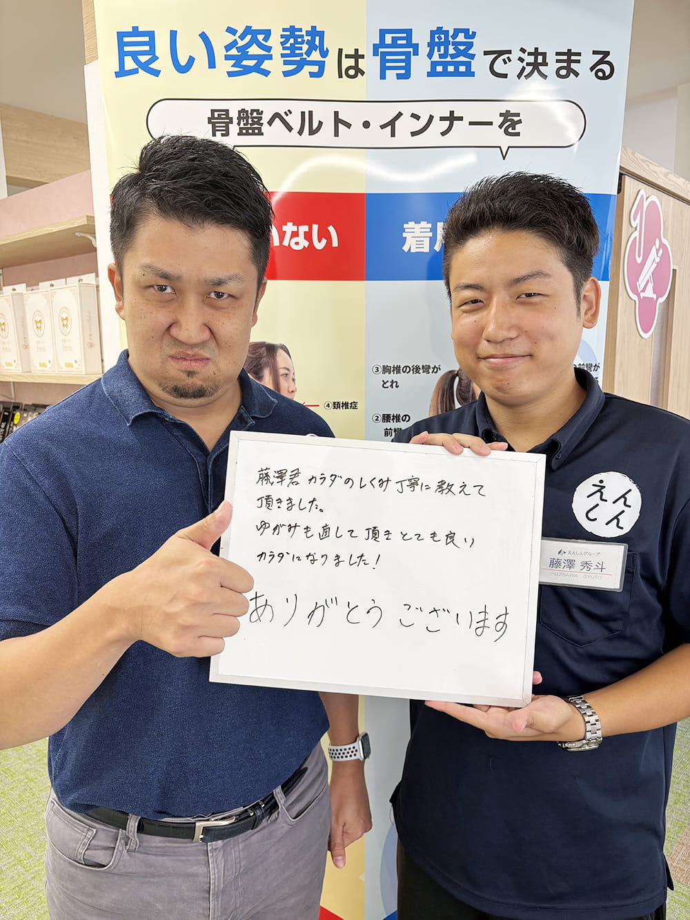 施術後の感想パネルを手にした患者が、制服姿のスタッフと笑顔で記念撮影している様子